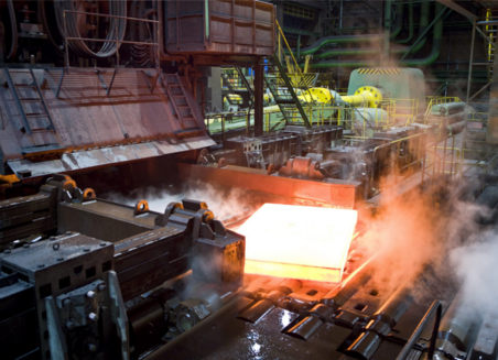 A large glowing piece of metal comes out of a machine. It steams. 
