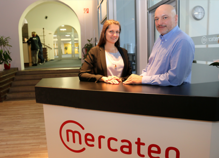 Two Mercateo employees stand behind a counter with the company logo in the company's offices.