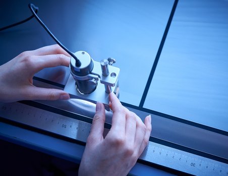 A pair of hands cut foils on a work table with an electronic cutter and ruler.